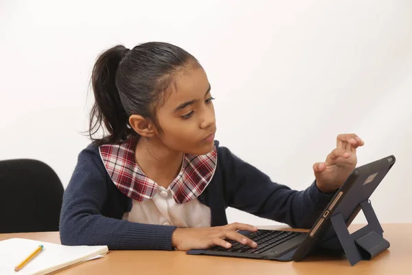 Esmer kız iPad cihazıyla ödev ve dersler veriyor ve kameraya gülümsüyor.