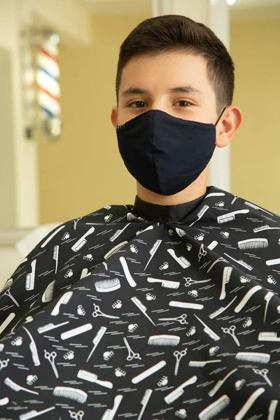 Berber dükkanındaki mutlu Latin çocuk, salgın yüzünden koruyucu maske takıyor.