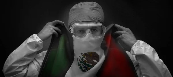 コロナウイルスから身を守る服を着た医師はメキシコの国旗を口の保護に使いメキシコの国旗を持つ医師は — ストック写真