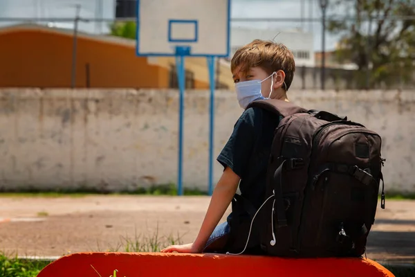 Koruyucu maskeli çocuk, üzgün, okul bankında oturuyor.