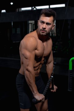 Erkek atlet yeşil simülatörün yanında spor salonundaki deltoid, pazı ve triseps kasları için egzersizi nasıl yapacağını gösteriyor. Seksi erkek vücut geliştirici, spor yaşam tarzı, ev sporları.