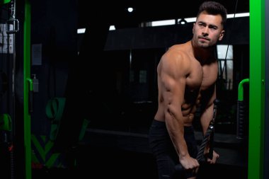 Erkek atlet yeşil simülatörün yanında spor salonundaki deltoid, pazı ve triseps kasları için egzersizi nasıl yapacağını gösteriyor. Seksi erkek vücut geliştirici, spor yaşam tarzı, ev sporları.