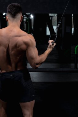 Erkek atlet yeşil simülatörün yanında spor salonundaki deltoid, pazı ve triseps kasları için egzersizi nasıl yapacağını gösteriyor. Seksi erkek vücut geliştirici, spor yaşam tarzı, ev sporları.