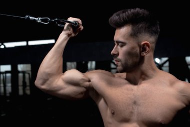 Erkek atlet yeşil simülatörün yanında spor salonundaki deltoid, pazı ve triseps kasları için egzersizi nasıl yapacağını gösteriyor. Seksi erkek vücut geliştirici, spor yaşam tarzı, ev sporları.