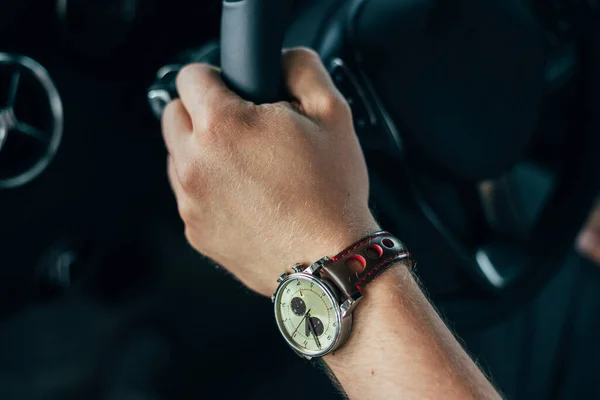 male hand with a clock holds the steering wheel of a car