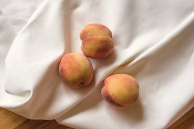 Olgun şeftaliler yumuşak keten beyazı kumaşlarda yatıyor.