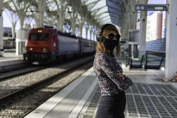 A young beautiful girl wearing the face mask is waiting for the train alone at the train station in Lisbon, Portugal
