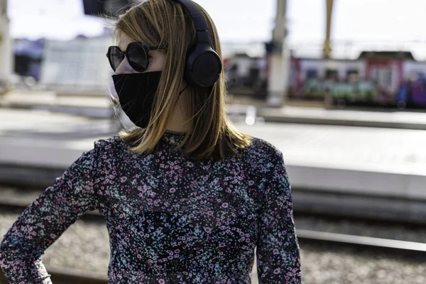 A young beautiful girl wearing the face mask is waiting for the train alone at the train station in Lisbon, Portugal