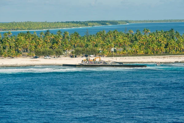 A beautiful view of a small Atoll in the middle of the south Pacific Ocean from the cruise ship deck while the officers and the crew members of a cruise ship are rescuing another small sailing boat.