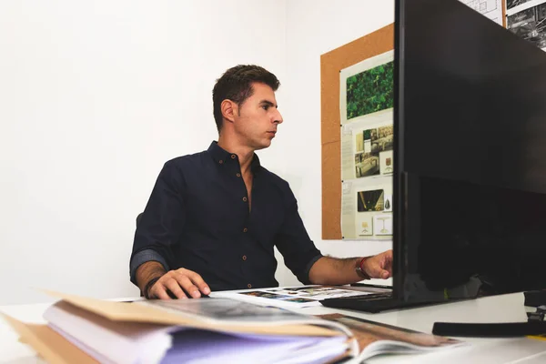 A young male architect working on a project in his office in Lisbon, Portugal. Young man working smart using the desktop computer while working on interior design project in his studio
