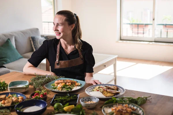 Young attractive swedish food blogger posing in front of a table full of food dishes. Young girl sitting in front of a wooden table eating vegetarian food and healthy dishes. Vegetarian lifestyle