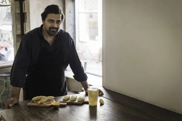 A charming cook presenting new dishes creation in a small restaurant in Lisbon. Joyful restaurant owner showing the new Empanada plates and the Portuguese Bifana at lunch in his own coffee shop