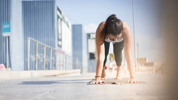 Sporty young woman doing Yoga exercises using a gym mat along the beach in Lisbon, Portugal. Playful woman working as freelance Yoga teacher doing fitness workout on the beach at sunset. Healthy life