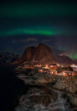 Norveç 'te ışıklandırılmış balıkçı köyü üzerinde Aurora borealis
