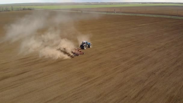 Vista aérea do poderoso trator azul com grande esforço no gancho realizando lavoura para semear culturas com cultivador vermelho — Vídeo de Stock