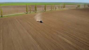Çiftçinin klasik mavi traktördeki hava görüntüsü güneşli bir günde kahverengi tozlu toprak ekiyor.