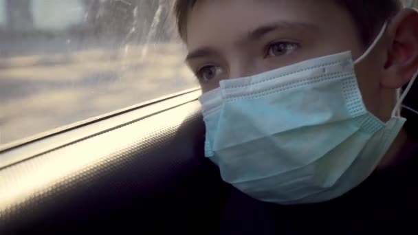 Ritratto giovane ragazzo in maschera medica guarda fuori dal finestrino auto in movimento sulla strada. Autoisolamento in quarantena — Video Stock