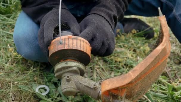 Человек садовник в черных рабочих перчатках починить или починить электрический газонный триммер для стрижки травы — стоковое видео