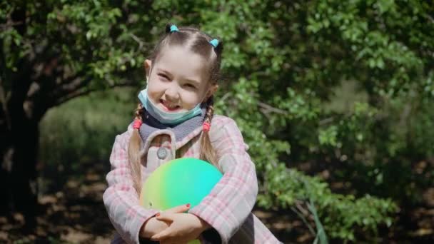 Portret van klein schattig meisje in beschermend masker voor coronavirus preventie met het spelen bal in de handen — Stockvideo