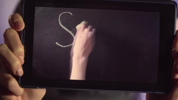 年轻女子的近视显示了平板电脑的屏幕，其中女性的手用粉笔写在黑板上的呼吁文字，以阻止考拉病毒的传播 — 图库视频影像