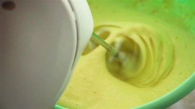 Elektrikli mikserin yakın çekim videosu lezzetli yemek malzemelerinden birini yaptığı için sarı yumurtayı çırpıyor.