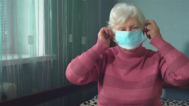 Mujer mayor se pone mascarilla facial para protegerse del brote de coronavirus y la pandemia en casa — Vídeo de stock