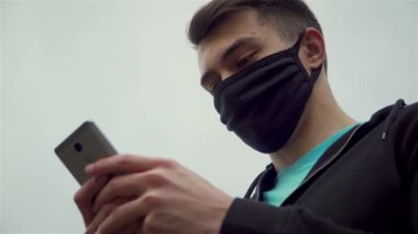 Korunan tıbbi maskeli bir adamın portresi Corona virüsü salgını başladığında cep telefonunda mesajlar yazıyordu.