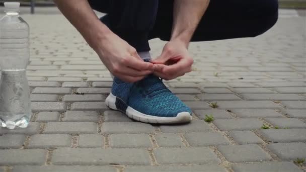 Hombre ata los cordones en los zapatos deportivos durante el ejercicio de carrera cardiovascular y la botella de agua está cerca — Vídeos de Stock