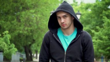 Spor ceketli, kafasında kapüşonlu, kameraya bakıp parkta duran çekici bir adamın portresi.