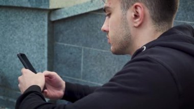 Kafkas asıllı Amerikalı genç adam akıllı telefon cihazı tutuyor. Şehir parkındaki merdivenlerde SMS mesajı yolluyor.