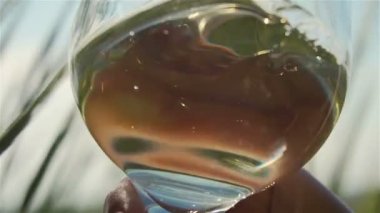 Beyaz köpüklü şarap yeşil çimlerin üzerinde camda sallanıyor ağır çekimde arka planda.