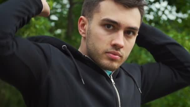 Retrato de joven caucásico guapo con apariencia de modelo quitarse la capucha de su chaqueta de la cabeza y mira con confianza a la cámara — Vídeos de Stock