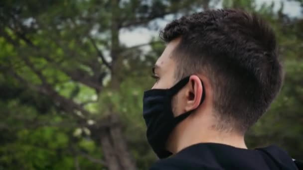 Närbild av unga kaukasiska turist man bär skyddande ansiktsmask promenader i stadsparken under coronavirus pandemi — Stockvideo