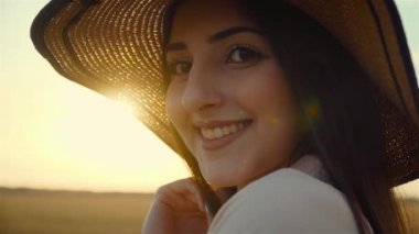 Güzel bir kadın portresi. Elbiseli ve şapkalı. Gün batımında ışık ışınlarıyla kameraya bakıyor.