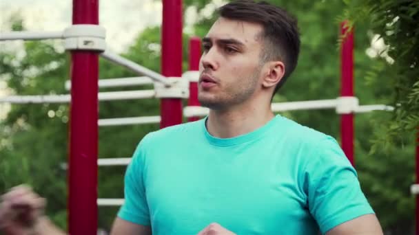 Retrato de homem jovem amassa músculos de seus braços e costas no pátio esportivo para a realização de exercícios de força em barras horizontais — Vídeo de Stock