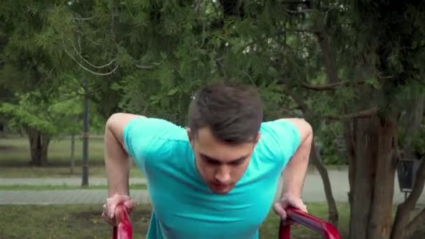 Спортивный кавказский мужчина с темными волосами, тренирующийся в открытом спортивном зале днем и подтягивающийся на тренировочной раме — стоковое видео