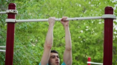 Güzel atletik genç adam spor sahasında antrenman yapmak için yatay bara yanaşıyor.