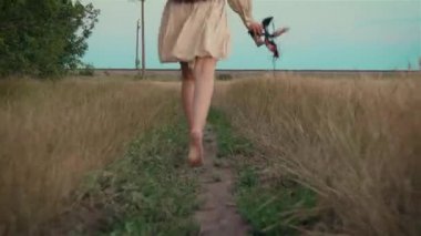 Çıplak ayaklı kadın bacaklarını kırsal alanda ya da elinde sandaletlerle çayırda koşarken kapat.