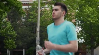 Gün batımında elinde bir şişe su olan sporcu. Parkta koşan koşucunun portresi. Dışarıda egzersiz yap.