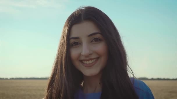 Atractiva joven mujer mirando a la cámara con sonrisa y sintiéndose perfectamente en el campo amarillo bajo el cielo azul en verano — Vídeo de stock