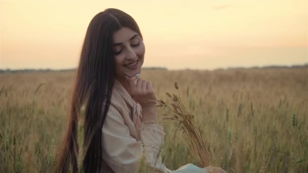 Porträt eines hübschen Mädchens im Sommerkleid mit Weizenstacheln in der Hand. Junge schöne Frau mit charmantem Lächeln — Stockvideo