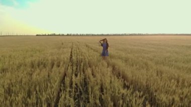Akşamları kuru buğday tarlasında yürüyen beyaz bir kadının videosunu çekiyor.
