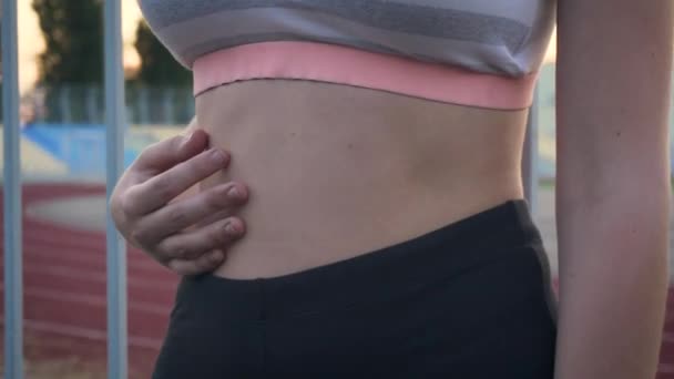 Sportlich fitte Frau in Sportbekleidung berührt ihren Bauch und atmet nach Fitnessübungen tief durch — Stockvideo
