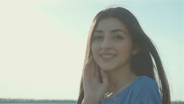 Mladá šťastná brunetka žena dotýká její vlasy na žluté pšeničné pole večer na pozadí slunce svítí — Stock video