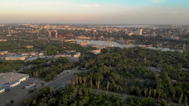 Vista aérea de la ciudad con coches y edificios en la calle y el río con astilleros con grúas en ella — Vídeos de Stock