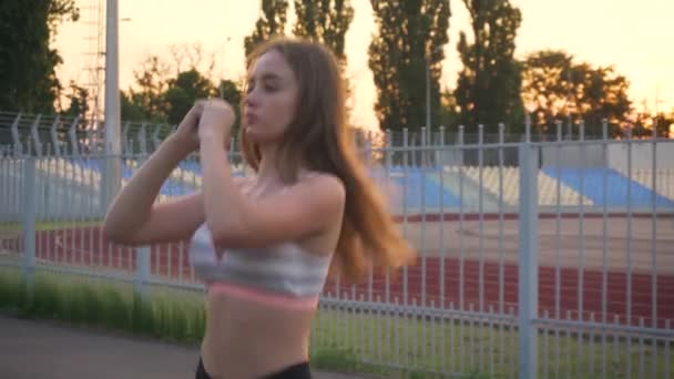 Großaufnahme einer fitten und gesunden jungen Frau in schwarzer Sportbekleidung, die im Freien in der Nähe eines geschlossenen Stadions Übungen für Quarantäne macht — Stockvideo