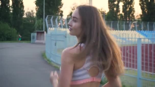 Последующий снимок молодой спортсменки, быстро бегающей возле закрытого стадиона, подтянутой девушки в черной спортивной одежде — стоковое видео