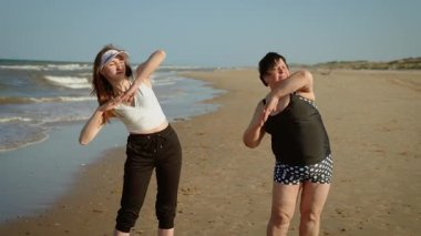 Kızlar kumlu sahilde yan yatıyorlar. Deniz kıyısında esneme egzersizi yapan kadınlar. Kadınlar cesetleri okyanus dalgalarının yanında ısıtıyorlar. Dişiler deniz kenarında birlikte egzersiz yapıyor.