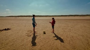 Çocuklar kumsalda birlikte top oynuyorlar. Gençler dışarıda oyun oynarken top oynuyorlardı. Erkek ve kız parlak gökyüzünün altında eğlenceli top aktivitelerinin keyfini çıkarıyorlar.