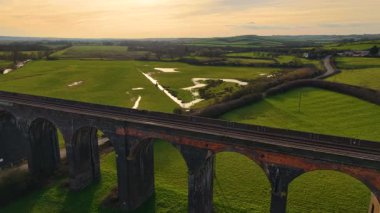 Turuncu gökyüzüne karşı demiryolu viyadük manzarası. Doğayı çevreleyen panoramik manzaralı eski viyadük üzerinde güzel bir gün batımı. Tarihsel noktalar, ünlü bölge, doğadan geçen ulaşım yapısı.